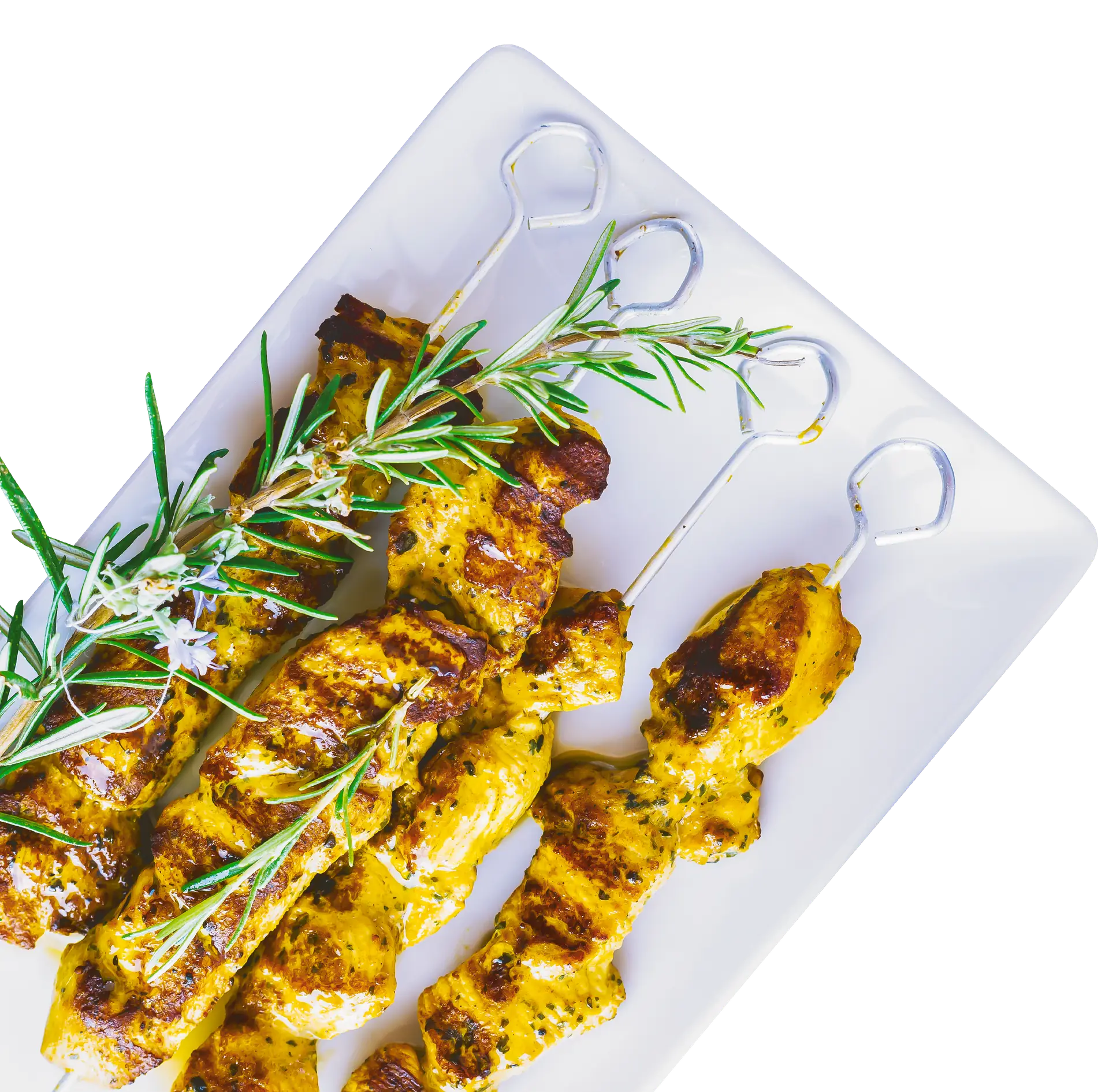 Quatre brochettes de poulet shish-taouk dorées sur un plat blanc carré, garnies de branches de romarin
